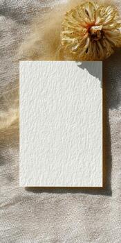 Minimalist flat lay composition on textured white linen featuring blank card and dried flower photo