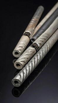 Several metal rods, varying in color and texture, lie on a dark surface, showing intricate designs and reflections photo