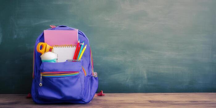 A fully packed school backpack with supplies in front of a chalkboard. photo