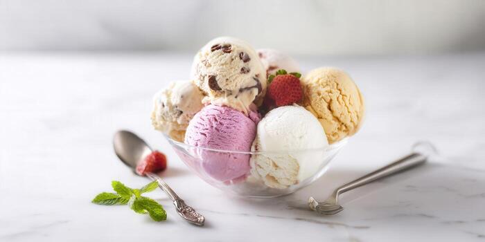 Assorted ice cream scoops in a clear bowl with fruit and mint on a marble surface. photo