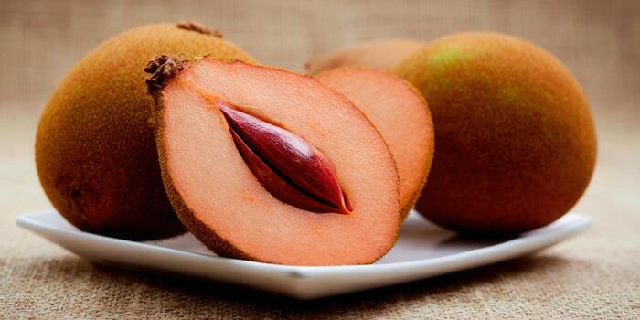 Sapodilla fruit, cut open to reveal its fleshy inside and seed on a white plate, ready to eat. photo