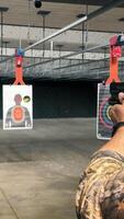 Man Practicing at Indoor Shooting Range, A man in camo attire aiming a handgun at targets in an indoor shooting range. video