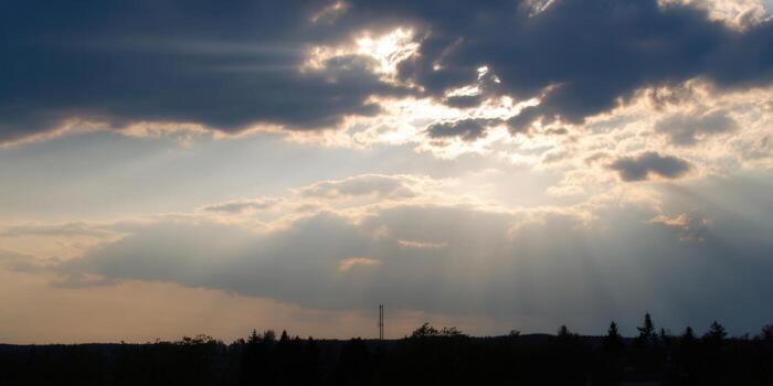 The sun's rays pierce through the clouds, casting a beautiful light over the trees. photo