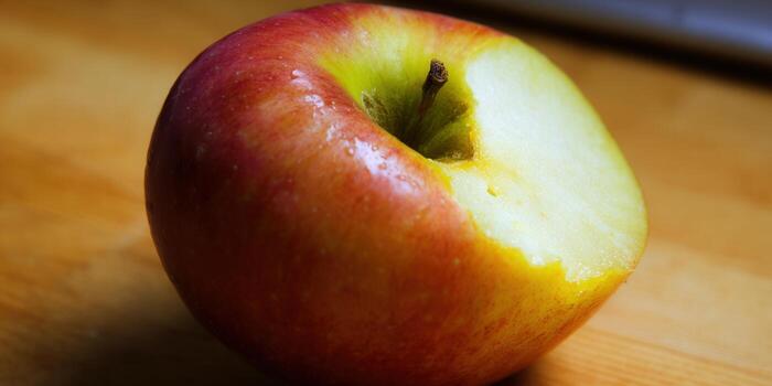 A fresh, crisp red apple with a bite taken out of it, sitting on a wooden surface. photo