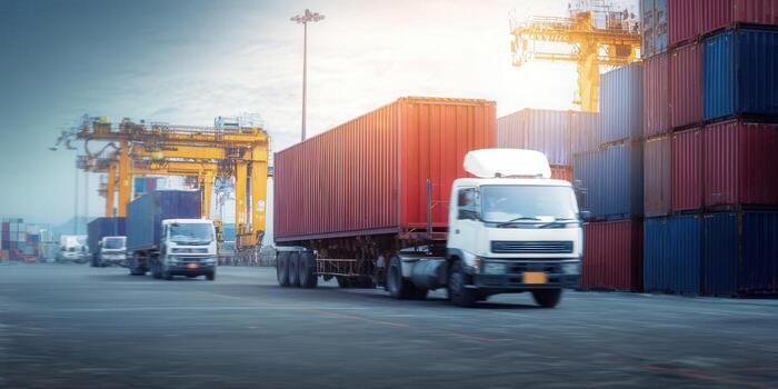 Truck carrying a shipping container drives through a busy port, ready for delivery. photo