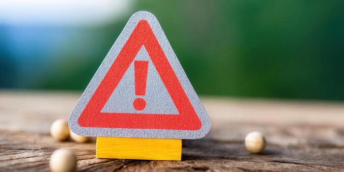 A warning sign with an exclamation mark on a wooden surface with a green background. photo