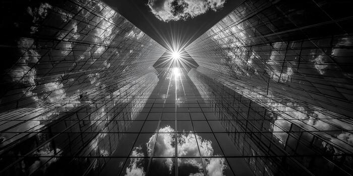 The imposing skyscrapers stand tall, reaching up towards the bright sun in a striking, monochromatic image. photo