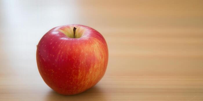 A close-up shot of a vibrant, red apple on a wooden surface. photo
