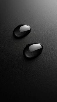 Two distinct, clear water drops resting on a dark, subtly textured surface, with soft reflections photo
