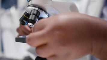 stänga upp av forskare fokusera på en mikroskop med prover i kemi labb. använder sig av observation verktyg med bricka för diagnostik, molekyl analys och upptäckt. optik i biovetenskap. kamera b. video