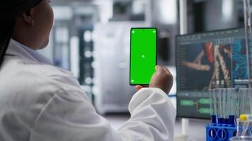 African American female scientist performs research with green screen in laboratory. Using smartphone display and conducting an experiment for biotechnology analysis. Clinical science. Camera B. video
