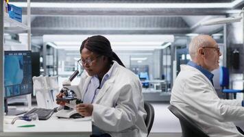forskare analyserar prover i laboratorium miljö med mikroskop och kemikalier. kvinna expert- framåt genetik forskning, kombinerande laboratorium analys med biokemi studier. kamera b. video