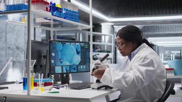 africano americano mulher analisando molecular amostras dentro uma bio laboratório, usando profissional microscópio. cuidados de saúde e bioquímica experimentos representar científico método e descoberta. Câmera uma. video