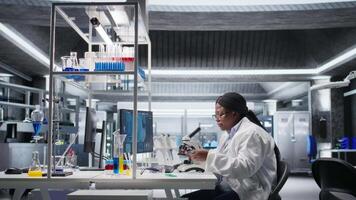 Researcher using microscope and specimen tray in laboratory workspace. Optical instrument, lens system and magnifying glass support clinical testing and biotechnology for healthcare. Camera A. video