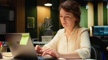 kvinna chef engagerad i skrivning anteckningar för en presentation på henne bärbar dator, extrahera grundläggande slingor från finansiera dokument och framställning en sammanfattning för företag mål och kommande uppgifter. kamera a. video