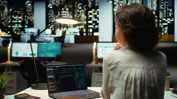 professionell arbetstagare i kontor monitorer stock trender och ljusstake diagram på bärbar dator, använder sig av data analys, prognostisering och finansiera strategi till optimera handel och uppnå inkomst mål. kamera a. video