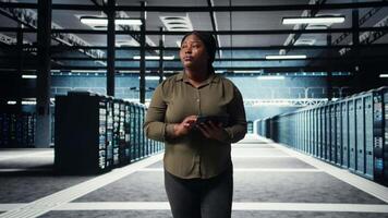 datos centrar ingeniero monitores datos centrar métrica en tableta a mejorar aparejos Operacional eficacia. trabajador camina mediante servidor granja filas, utilizando analítica en dispositivo a predecir actuación, cámara un video