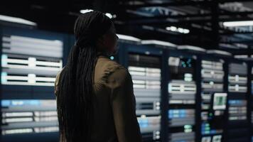 data Centrum systemet administratör övervakar den redskap till upprätthålla sömlös operationer. afrikansk amerikan kvinna promenader i server nav, håller på med nätverk förvaltning för ökade upptid, kamera b video