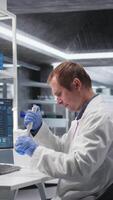 Vertical Male scientist handles pipette with droplet over jar during procedure in the lab. Mixture preparation supporting genetics research, nanotechnology and solutions through analytical methods. Camera A. video