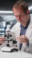 Vertical Employee studying sample tray under the microscope for research study in a lab, sliding the cellular investigation and supporting genetics research. Advanced analysis for healthcare. Camera A. video
