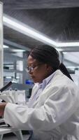 vertical africano americano químico analisando molecular amostras dentro uma laboratório, usando profissional microscópio. cuidados de saúde inovação e bioquímica experimentos representar científico método e descoberta. Câmera uma. video