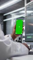 vertical negro experto utilizando croma llave pantalla para laboratorio estudiar en teléfono inteligente, trabajos con experimentar datos para molecular ciencia. avanzado investigación, farmacología y biotecnología descubrimiento. cámara una. video