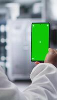 vertical africano americano hembra científico realiza investigación con verde pantalla en laboratorio. utilizando teléfono inteligente monitor y conductible un experimentar para biotecnología análisis. clínico ciencia. cámara b. video