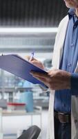 Vertical Man handwriting notes on clipboard for research study results in a chemistry lab, researcher conducting an experiment for biochemistry, nanotechnology and diagnostics. Camera A. video