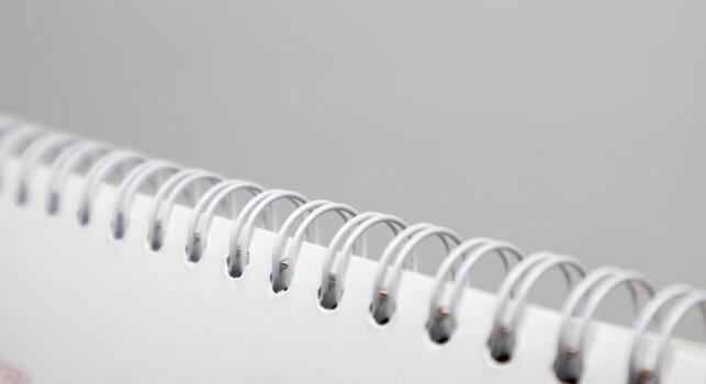A close-up, abstract shot of the white plastic spiral binding of a notebook or calendar against a simple, light gray background. The focus is on the repeating rings. photo