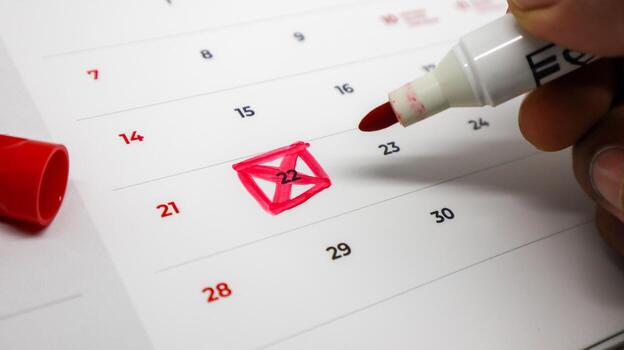 A hand uses a red marker to cross out the number 22 on a calendar, representing the concept of a completed deadline, task, or event. photo