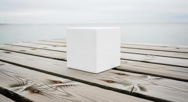 A white cube sits on a weathered wooden dock with a serene lake and sky in the background photo