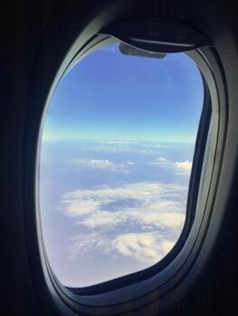 Scenic view from an airplane window seat showing white fluffy clouds and clear blue sky during flight. photo