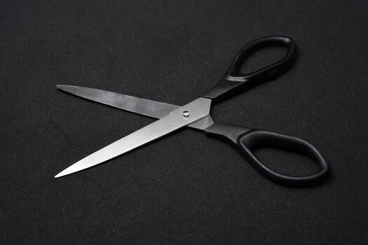 Minimalist flat lay of two classic stationery scissors on a dark, textured black background. This image emphasizes clean lines, geometric shape, and the metallic sheen of the blades. photo