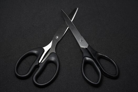 Two sharp stationery scissors isolated on a pure black background. A simple and clean composition, perfect for illustrating concepts of cutting, crafting, office work, or back-to-school themes. photo