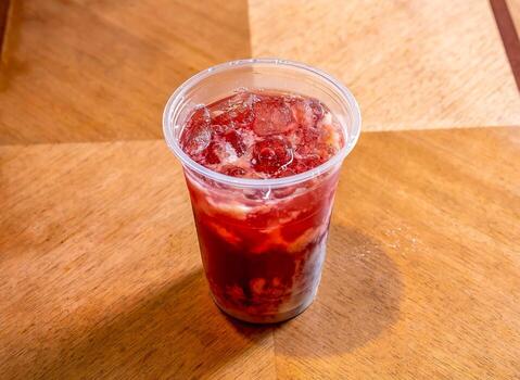 Iced Raspberry Lemonade Drink with White Foam Layer and ice cube in a Plastic Cup on wooden table side view of cold beverage photo