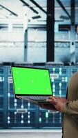 Vertical Developer in data center using green screen laptop to upgrade systems for increased stability. IT expert in server farm configuring hardware with mockup notebook for optimum performance, camera A video