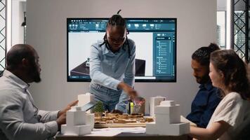 multiétnico arquitectura desarrolladores utilizando 3d modelos en lluvia de ideas reunión, muestra arquitectónico software a trabajo en estructural ciudad planificación. residencial proyecto para urbano desarrollo. cámara b. video