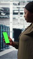 vertical software desarrollador utilizando aplicación en Bosquejo teléfono a cheque servidor cubo energía consumo. africano americano mujer utilizando verde pantalla teléfono inteligente en datos centrar a hacer engranaje chequeo, cámara un video