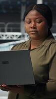 Vertical Technician in server room using laptop to upgrade rigs for increase in clients workload capacity. African american woman in data center configures equipment, improving processing speed, camera B video