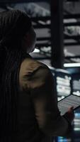 Vertical Data center system administrator monitors data center metrics on tablet to enhance operational effectiveness. IT expert in server room using analytics program to predict performance, camera B video