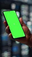 vertikal server nav programvara utvecklare användningar grön skärm smartphone till Kolla på handledning på på vilket sätt till uppgradera rigg. afrikansk amerikan kvinna i data Centrum följer guide på attrapp telefon till förbättra fart, kamera b video
