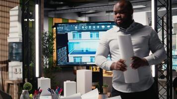 Black male engineer examining architectural 3D models for design, reviewing blueprints with strategic redevelopment project master plan. Residential area for infrastructure growth. Camera A. video