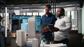 Multiethnic group of developers and contractors discussing urban housing models and blueprints layout revisions for upcoming residential development project. Smart city planning session. Camera A. video