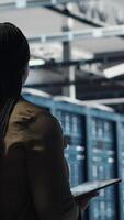 Vertical Woman walking through data center server rows, implementing advanced cooling and power management solutions. IT expert overseeing server farm, reducing energy consumption, camera B video