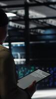 Vertical Engineer in data center using tablet to deploy secure server architecture. African american woman in server hub using device to do rollout of cybersecurity framework, camera B video