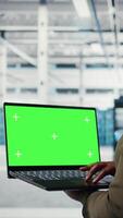 vertical computadora científico a trabajo utilizando verde pantalla ordenador portátil en datos centrar a cheque hardware para sistema estabilidad. gerente utilizando Bosquejo cuaderno a supervisar servidor granja engranaje, cámara un video