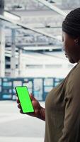 Vertical Worker using app on mockup phone to check server hub energy consumption. Admin using green screen smartphone in data center to receive instructions on implementing power management solutions. camera A video