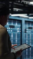Vertical Close up of data center programmer doing data analysis on tablet to upgrade infrastructure. African american woman in server room using device to manage storage systems datasets video