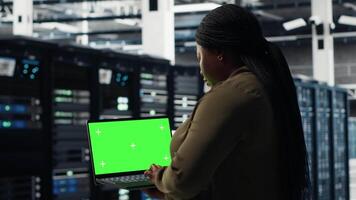 Server room admin uses green screen laptop to upgrade mainframes for increase in workload capacity. Data center worker configures gear with mockup notebook, improving processing speed, camera B video
