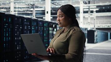 Data center workplace programmer using laptop to coordinate deployment of new server architecture. Server room worker using notebook to do rollout of cybersecurity framework, protecting data, camera A video